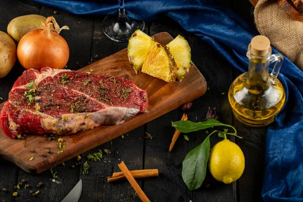 Rauw vlees op een houten plank met kruiden en specerijen, geserveerd met olijfolie, citroen en ananas — Stockfoto
