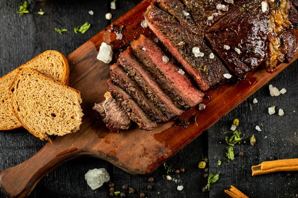 Barbacoa de carne en rodajas servida en una tabla de madera, filetes de canela y pan alrededor — Foto de Stock