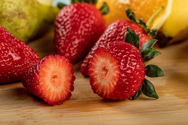 Rote frische Erdbeeren in Stücke geschnitten mit anderen Früchten auf einem Holzbrett — Stockfoto