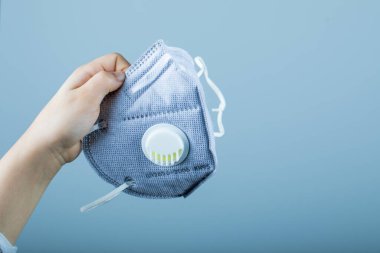Çocuğun elinde tıbbi maske var.