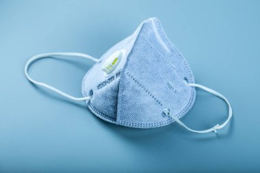 Mavi, modern bir tıbbi yüz maskesi mavi arka planda izole edilmiş.