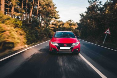 Ağaçların arasından geçen dağ yolunda kırmızı kovalayan araba.