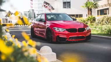 Boş şehir yollarında yeşil çimlerin üzerinde kırmızı model bir sedan.