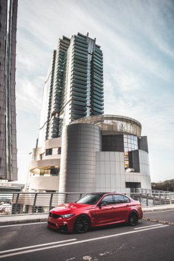 Modern bir konutun önünde kırmızı evrensel SUV, gökdelenler arasında sürüş