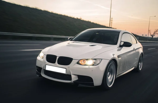 White sport car rush in the sunset time, front lights on,in the highlands — Stock Photo, Image