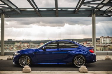 Modern bir otoparkta mavi bir sedan park ediyor.