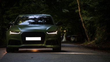 Karanlık çöktüğünde orman yolunda ağır çekimde giden siyah bir sedan.