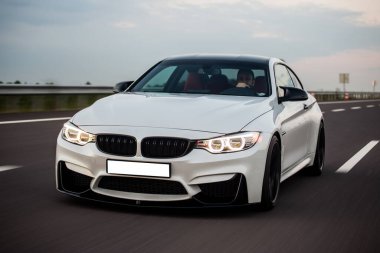 Beyaz sedan, sarı farlar alacakaranlıkta yanıyor.