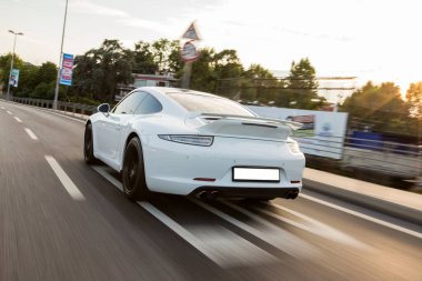 Beyaz spor araba gündüz ıssız tarlalarda aşırı hareket ediyor, arkadan bakıyor.