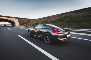 Gün batımında otobanda deniz mavisi spor araba sürüşü, arkadan görüş.