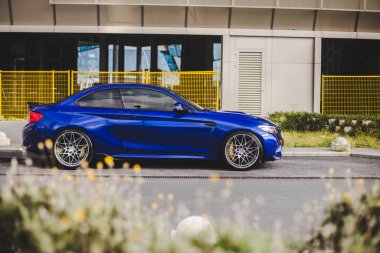 İş yerinin önünde mavi spor model bir sedan.