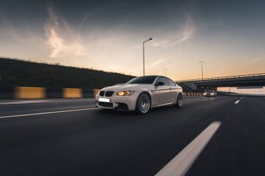 Beyaz modern sedan test sürüşü otoyolda, ön ışıklar açık