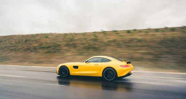 雲の下の高速道路で黄色の近代的な技術スポーツモデル車、後ろからの眺め — ストック写真