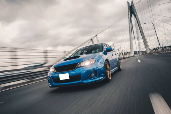 Синій спортивний автомобіль їде по автостраді через міст в штормову погоду, передні вогні увімкнені — стокове фото