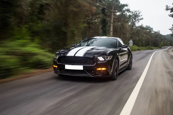 Zwarte auto met witte strepen op de bosweg, hoekzicht — Stockfoto