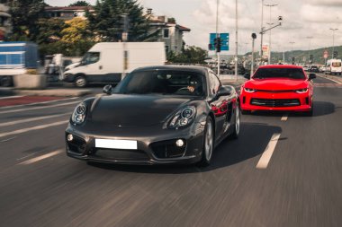 Kırmızı ve siyah süper arabalar şehir sokaklarında yarışıyor.