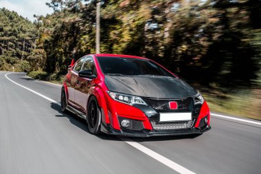 Siyah akortlu kırmızı mini sedan yolda ilerliyor.