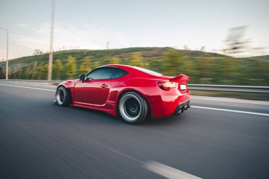 Kırmızı zarif spor araba manzarası yeşil arazide ilerliyor.