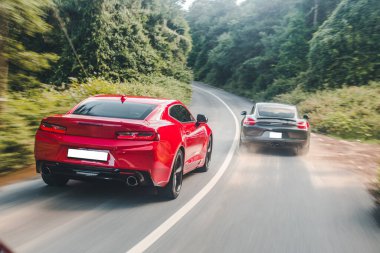 Kırmızı ve siyah spor arabalar birbirinin yanından geçiyor, arkadan görünüyor.