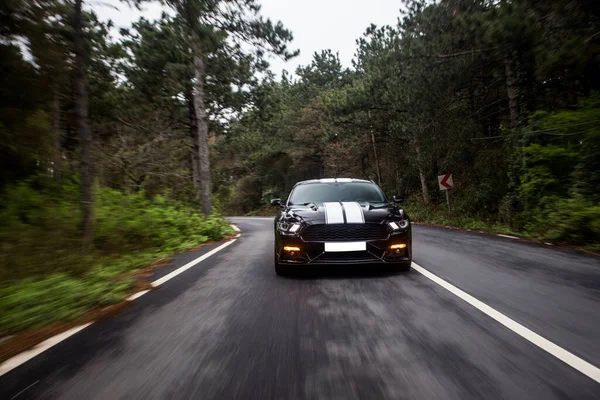 Black car with white stripes on the forest road — Stock Photo, Image