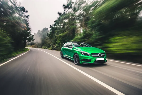 Mini auto sportiva verde che guida sull'autostrada in un tempo nebbioso piovoso attraverso la foresta — Foto Stock