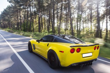 Ormanda siyah çatılı sarı spor bir sedan.