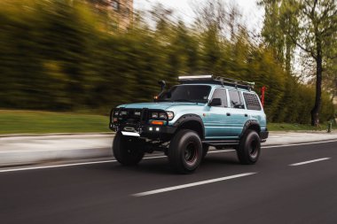 Kırsal yolda yeşil ağaçların arasından geçen mavi off-road kamyonu.