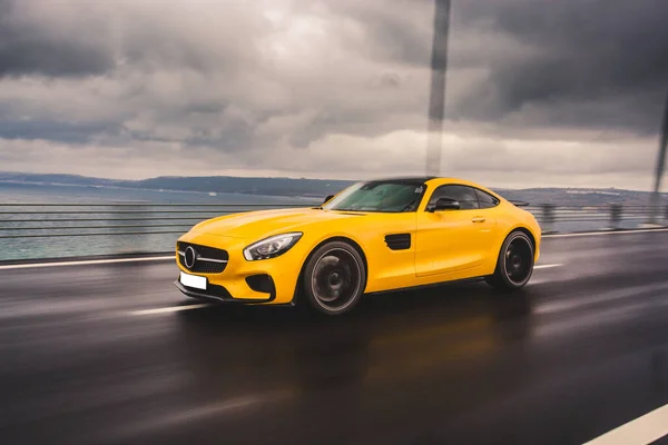 Auto-show deportivo amarillo en la lluvia sobre el asfalto húmedo bajo nubes oscuras — Foto de Stock