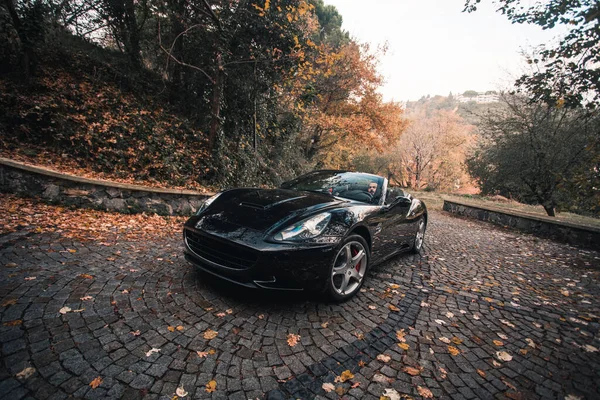 Черный роскошный автомобиль в осеннем лесу через осенние листья — стоковое фото
