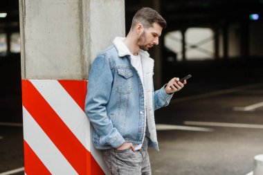 Moda ceketli bir adam şehrin otoparkındaki sütunun yanında duran bir telefonu tutuyor.