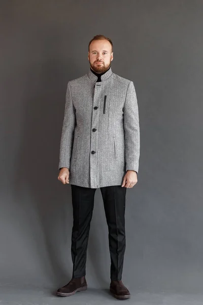Homem barbudo em um casaco cinza fica em um fundo cinza Imagem De Stock