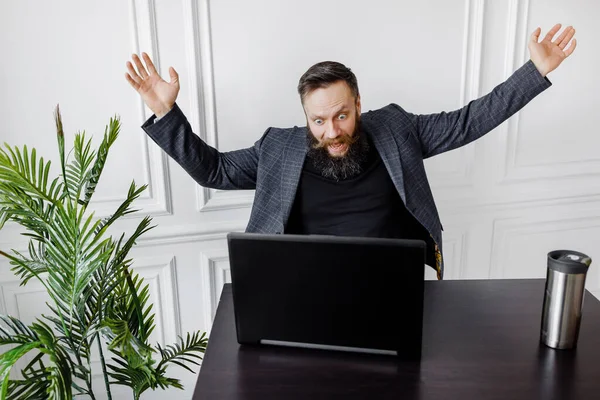 Mężczyzna w garniturze spogląda na coś strasznego i krzyczy do swojego laptopa w białym pokoju Obrazek Stockowy