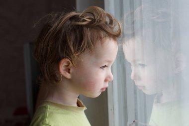 small boy sitting near window and thinking about something. He has beautiful great hair. Cute baby. clipart