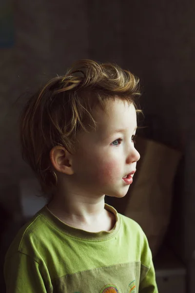 Niño pequeño sentado cerca de la ventana y pensando en algo. Tiene un pelo hermoso y estupendo. Lindo bebé . —  Fotos de Stock