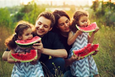 Neşeli pozitif aile dört piknik ve karpuz güneşli havalarda açık havada yemek. Kıvırcık güzel ikiz kız kardeş bir aperatif yemek yemek. Vejetaryen kavramı. Mutlu insanlar.