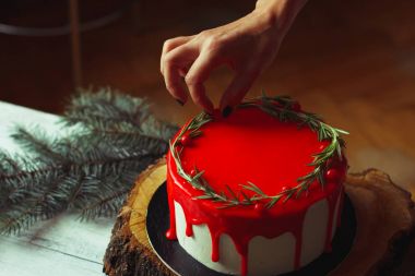 Holly Şubeler ve kestane ile eski Beyaz ahşap masa üzerinde rozmarine ve kırmızı meyveler ile kadının el tarafından işlem ev yapımı Noel kırmızı ganache pasta dekorasyon. Karanlık rustik tarzı.
