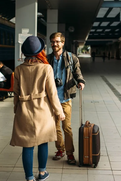 Woman meeting her boyfriend from his trip at the train station. Tourist Man with luggage and photo camers. Travel concept. Redhair girlfriend.