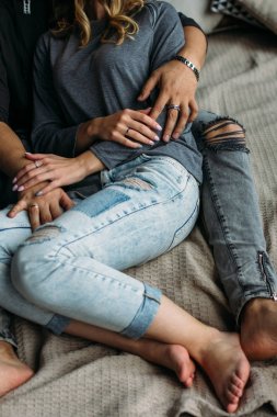 Cropped view of youngcouple embracing and relaxing on bed at home. Vintage casual look. Torn blue jeans. Winter time clipart