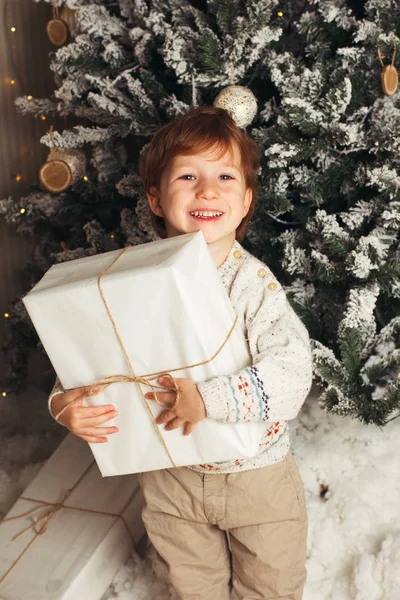Menino jovem caucasiano segurando presente de Natal na frente da árvore de Natal. Bonito menino sorridente feliz. Foto vertical — Fotografia de Stock