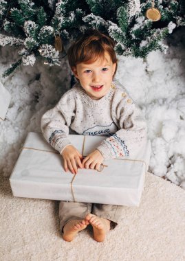Sevimli küçük çocuk hediyeler Noel ağacının etrafında bir kutu ile oturuyor. Sevimli sarışın beyaz toddler