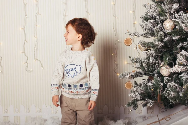 Menino bonito está sentado com um presente perto da árvore de Natal. A criança está feliz com o presente de Ano Novo. Caucasiano loira criança menino — Fotografia de Stock