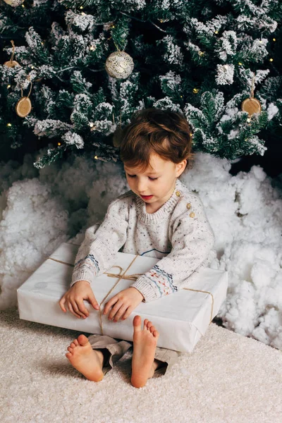 Bonito menino sentado com uma caixa de presentes ao redor da árvore de Natal. Adorável loira caucasiana criança — Fotografia de Stock