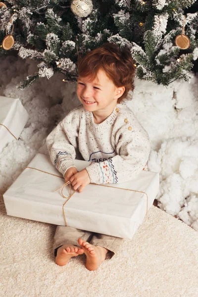 Bonito menino sentado com uma caixa de presentes ao redor da árvore de Natal. Adorável loira caucasiana criança — Fotografia de Stock