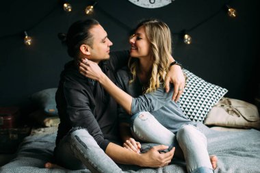 Erkek arkadaşımla birbirimizi gri battaniye ve yastık yatak üzerinde oturan dokunmadan girfriend. Işıklar, Romantik Oda rahat ve kavram seviyorum. Çift öpüşme ve gülümseyerek. İnsanlar kot pantolon