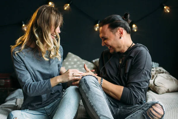 Young couple sitting on bed and laughing while tickling each other. Smiling happy people. Curly girlfriend. People in jeans — Stock Photo, Image