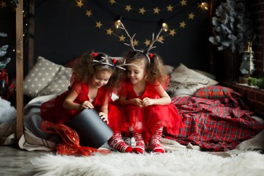 Çocuklar Noel hediyesi açma. Geyik boynuzları kafasına iki küçük todder kız. Rahat Oda yatakta oturup kırmızı İkizler Giydir.