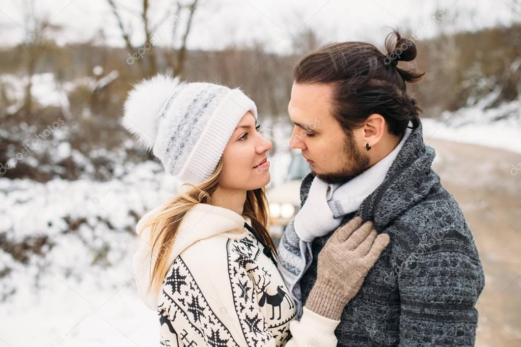 winter snow couple love story. Beautiful girl in cozy hat and handsome bearded man hugs each other. pullover with traditional winter ornament