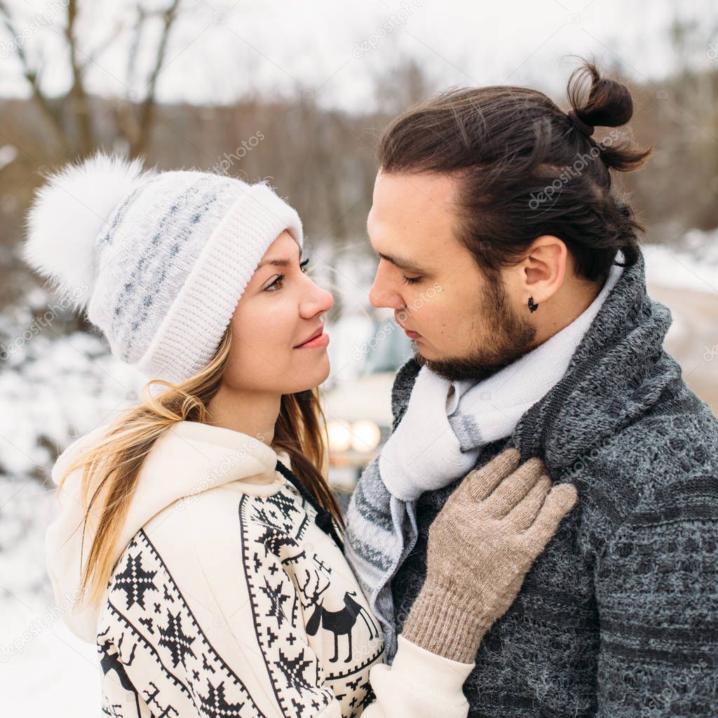 winter snow couple love story.Beautiful girl in cozy hat and handsome bearded man hugs each other. pullover with traditional winter ornament. Square picture