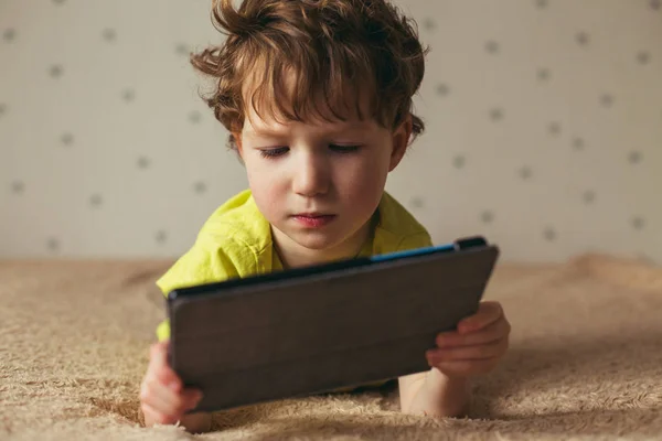 Kleiner süßer Junge in grünem T-Shirt, der auf einem Tablet Spiele spielt und sich Cartoons ansieht. Kleinkind mit Tablet. — Stockfoto