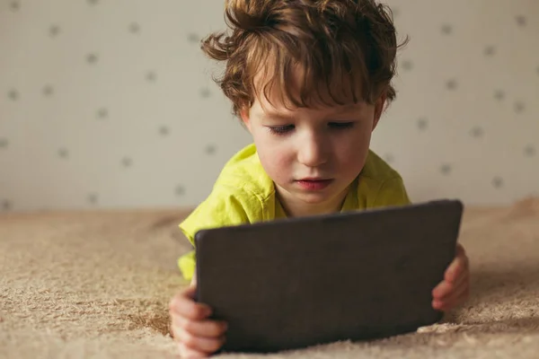 Kleiner süßer Junge in grünem T-Shirt, der auf einem Tablet Spiele spielt und sich Cartoons ansieht. Kleinkind mit Tablet. — Stockfoto